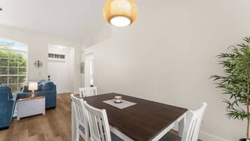 A dining area with a wooden table and white chairs, a hanging light fixture, and a potted plant.