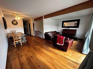A living room with a wooden floor, a brown leather sofa, a dining table with chairs, a ceiling fan, and a piano. - spacious sunny full house in west hillhurst (Calgary)