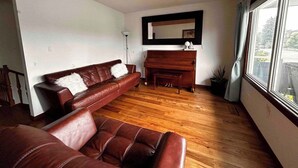 A living room with a brown leather sofa, a wooden piano, and a large window. - spacious sunny full house in west hillhurst (Calgary)