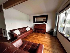 A living room with a brown leather sofa, a wooden piano, and a large window. - spacious sunny full house in west hillhurst (Calgary)