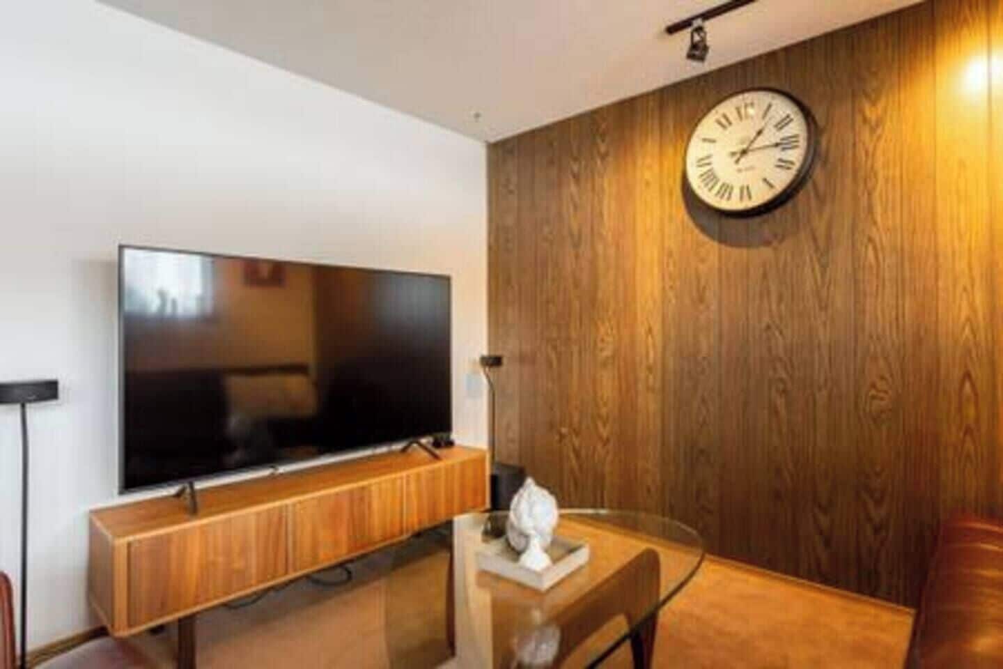 Una sala de estar moderna con un televisor de pantalla plana montado en una pared de madera, una mesa de centro de vidrio y un mueble de madera.