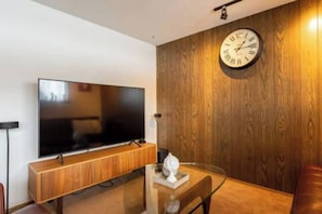 A modern living room with a flat-screen TV mounted on a wooden wall, a glass coffee table, and a wooden cabinet. - spacious sunny full house in west hillhurst (Calgary)