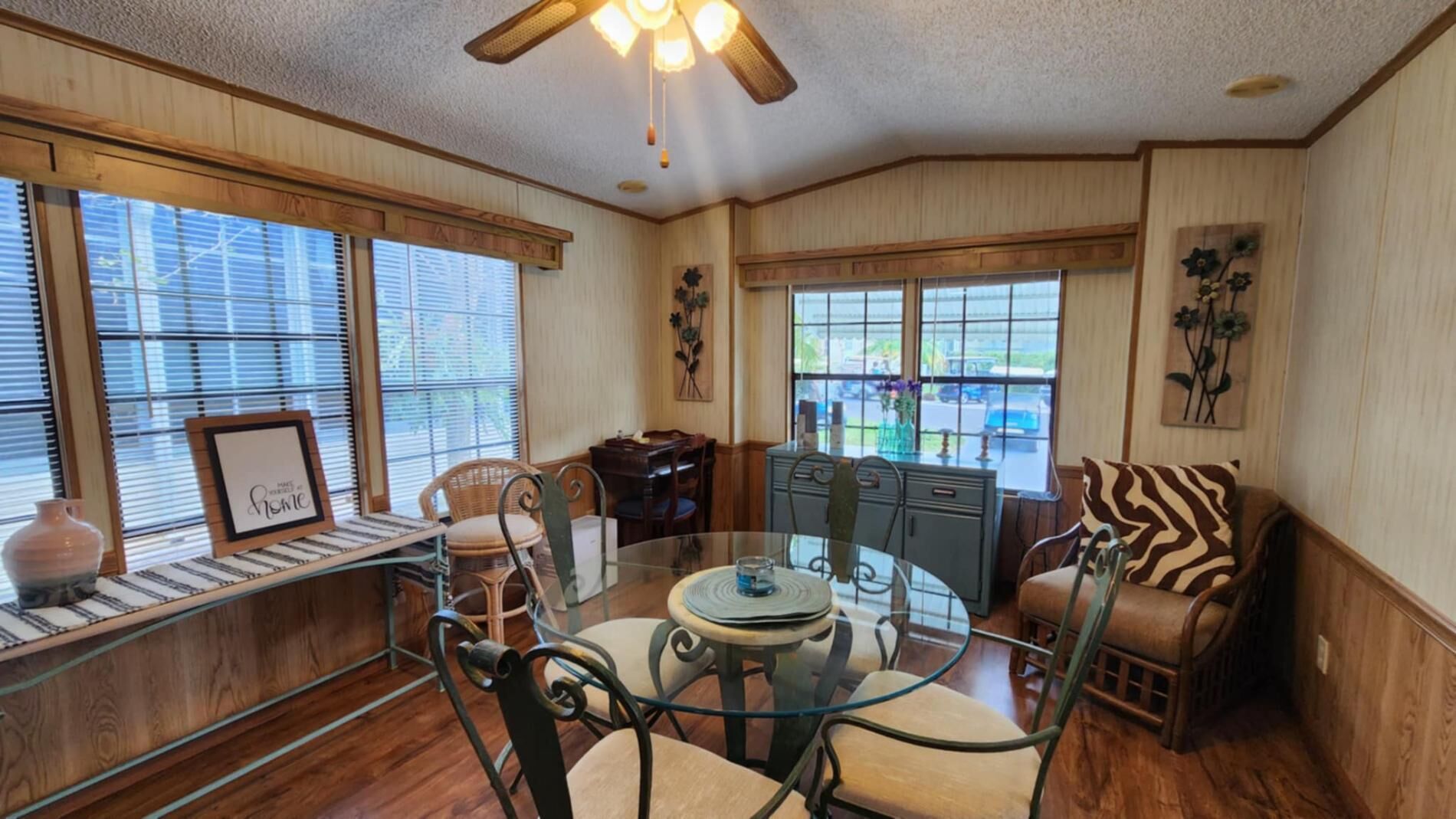 A dining area with a round glass table, chairs, a bench, and a window with blinds.