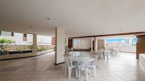 A spacious outdoor terrace with multiple dining tables and chairs, surrounded by potted plants and a view of the cityscape. - Apartment With City Views in Rio Vermelho Jdo0104 (Salvador)