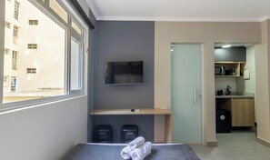 Ein Hotelzimmer mit Bett, Wandfernseher, kleinem Schreibtisch und Blick nach draußen.