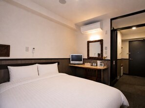 A hotel room with a bed, a television, a desk with a mirror, and a door leading to another room.