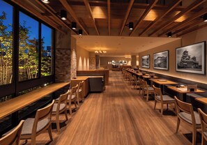 Un restaurante con mesas y sillas de madera, un muro de ladrillo y cuadros en la pared.