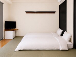 Un dormitorio minimalista con una cama, un televisor sobre un mueble y una puerta oscura.