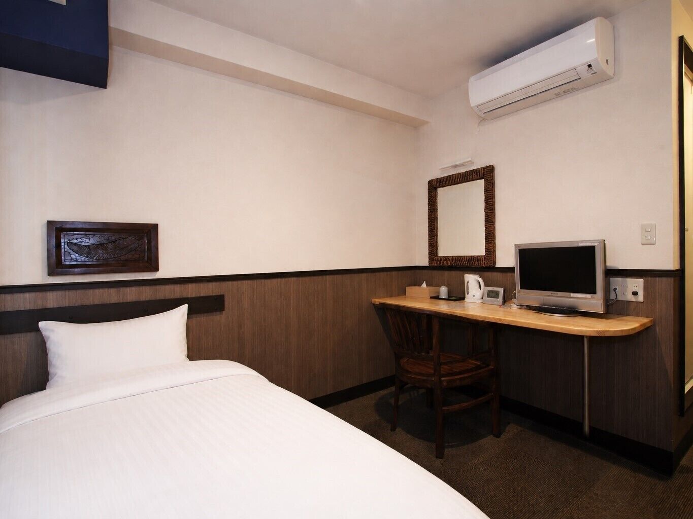Habitación de hotel con cama, escritorio, silla, televisión y aire acondicionado.