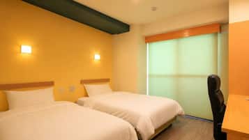 A hotel room with two beds, a desk, and a window with blinds.