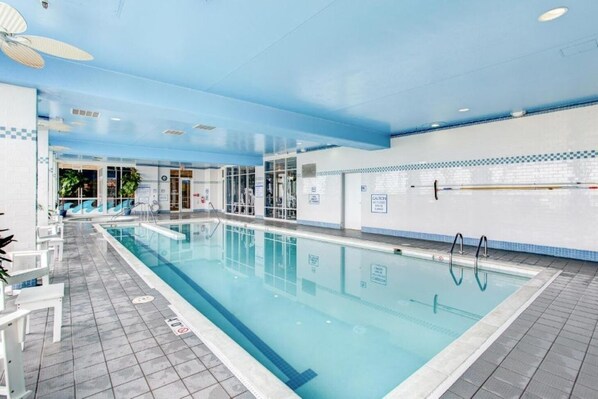 Piscina interior com água cristalina, chão ladrilhado e ventiladores no teto.