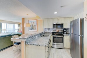 A kitchen with granite countertops, stainless steel appliances, and a breakfast bar. - Virginia Beach | Ocean View Getaway | Pool & Beach | 2BR (Virginia Beach)