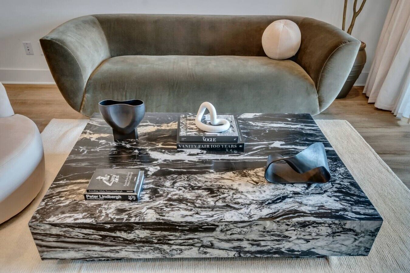 A modern living room with a sofa, a coffee table with books and decorative items, and a marble-patterned rug.