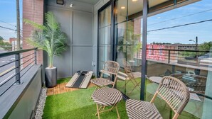 A balcony with a green artificial turf, a large potted plant, and wicker chairs. - Modern Loft/Walk To Stadiums/Free Parking! (Atlanta)