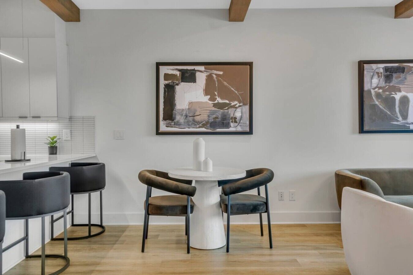 Eine moderne Küche mit weißen Schränken, einer Bar mit schwarzen Barhocker und zwei gerahmten abstrakten Bildern an der Wand.