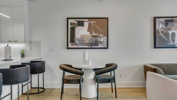 Eine moderne Küche mit weißen Schränken, einer Bar mit schwarzen Barhocker und zwei gerahmten abstrakten Bildern an der Wand.