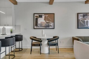Eine moderne Küche mit weißen Schränken, einer Bar mit schwarzen Barhocker und zwei gerahmten abstrakten Bildern an der Wand.