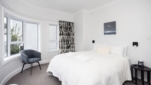 Een hotelkamer met een groot bed, een stoel, een raam en een schilderij aan de muur.