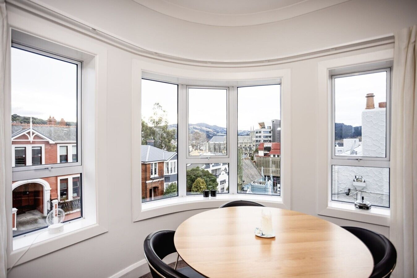 A room with a round table and four large windows offering a city view.