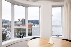 A room with a round table and a candle, large windows with a city view, and a white textured wall. - The Deco View, Warm Art Deco Apartment with Garage (Dunedin)