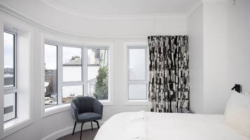 A hotel room with a large bed, a chair, a window with a view, and a curtain with a geometric pattern.