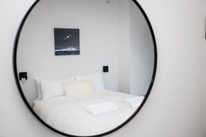 A bedroom with a bed, white pillows, a fluffy pillow, a white towel, a wall-mounted picture, and two wall-mounted speakers. - The Deco View, Warm Art Deco Apartment with Garage (Dunedin)