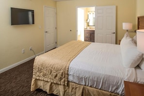 A hotel room with a bed, a TV, a door, and a bathroom visible through an open door.