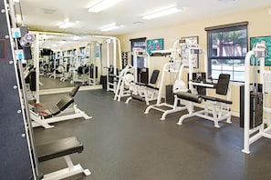 A gym with various exercise machines, mirrors, and a window.