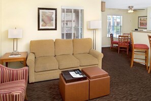A hotel room with a beige sofa, striped armchair, and a small table with a remote control.