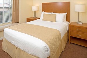 Une chambre d’hôtel avec un grand lit, deux tables de chevet, une fenêtre avec des stores et une lampe sur chaque table.