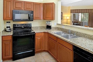 A kitchen with wooden cabinets, a black stove, a microwave, a coffee maker, and a sink.