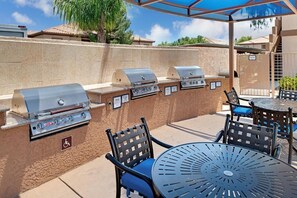 Un espace extérieur équipé d’un barbecue avec plusieurs postes de cuisson, d’un coin salon extérieur avec des chaises et une table, et d’un patio couvert.