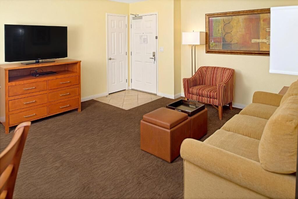 A living room with a TV, wooden cabinet, striped chair, ottoman, and a painting on the wall.