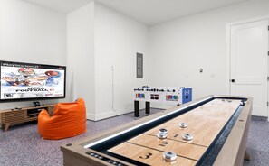 Una habitación con una mesa de fútbol de mesa, un televisor mostrando NCAA Football 11 y un pequeño sillón de peluche naranja.