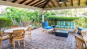 Eine Terrasse im Freien mit einem runden Tisch, Holzsesseln, einer Couch mit Streifenpolstern und einem Deckenventilator.