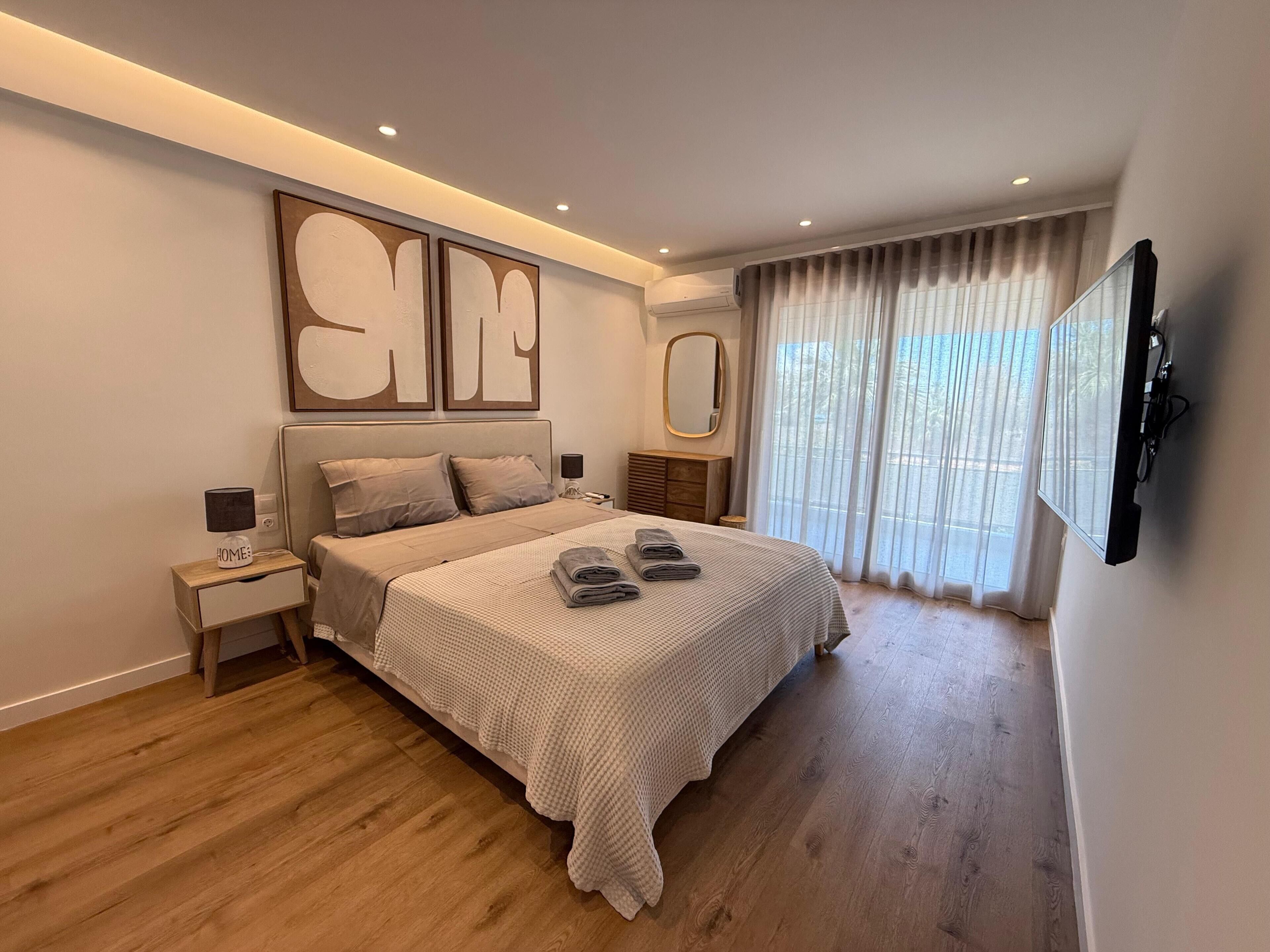 A modern bedroom with a large bed, a flat-screen TV, and a large window with curtains.