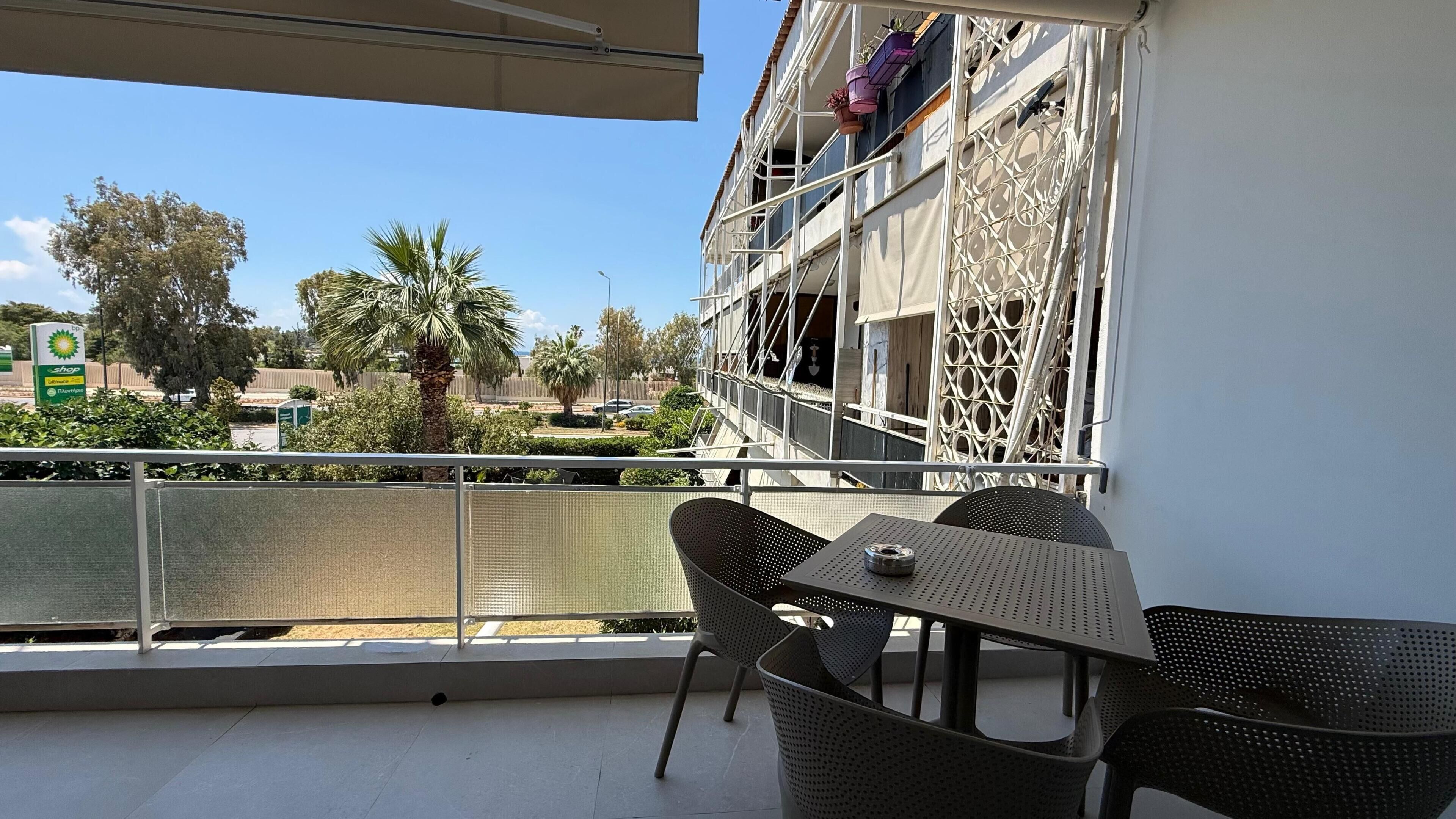 A balcony with a table and chairs, a view of a palm tree, and a building with scaffolding.