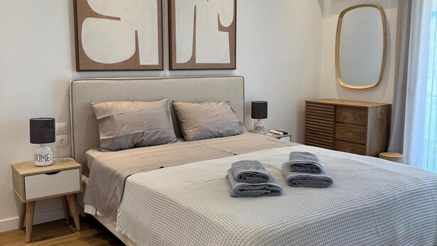 Quarto moderno com uma cama grande, mesas de cabeceira, um espelho e um ar condicionado fixado na parede.