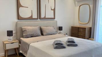 A modern bedroom with a large bed, bedside tables, a mirror, and a wall-mounted air conditioner.