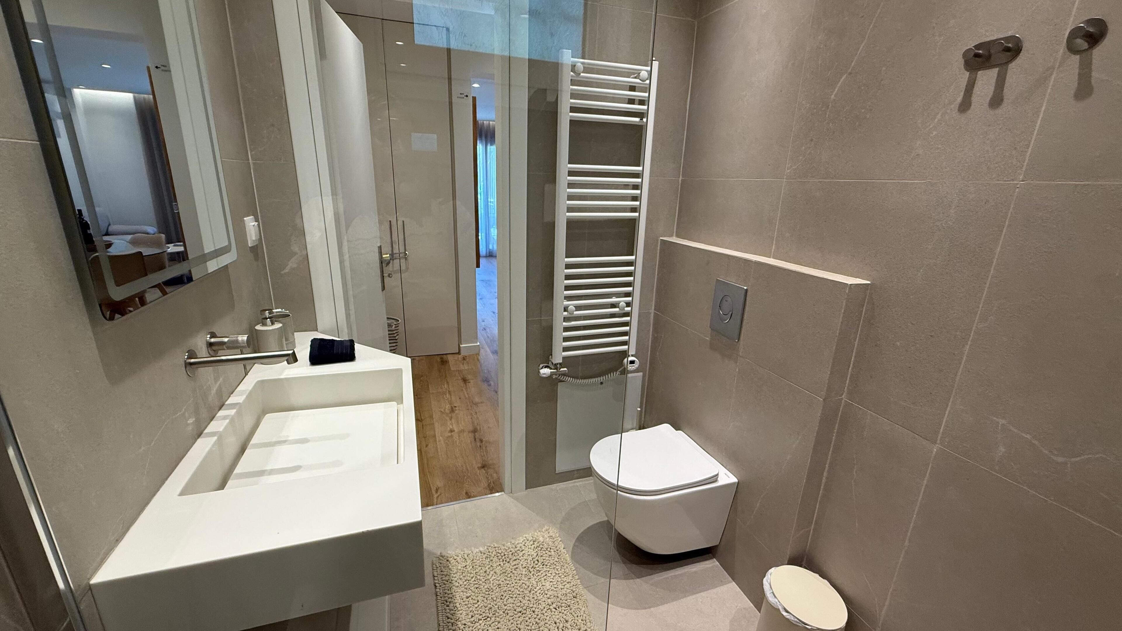 A modern bathroom with a white sink, a glass shower enclosure, and a white toilet.