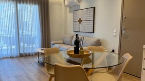 Uma sala de estar moderna com uma mesa de jantar de vidro, cadeiras bege, um sofá e uma janela grande com cortinas.