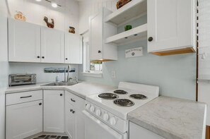 A kitchen with white cabinets, a stove, a sink, and a toaster. - Salt & Summit Coastal Cottage - Ogunquit Escape (Ogunquit)