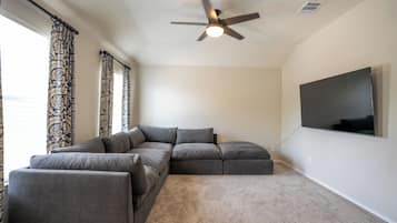 Una sala de estar moderna con un sofá modular, un ventilador de techo y un televisor de pantalla plana montado en la pared.