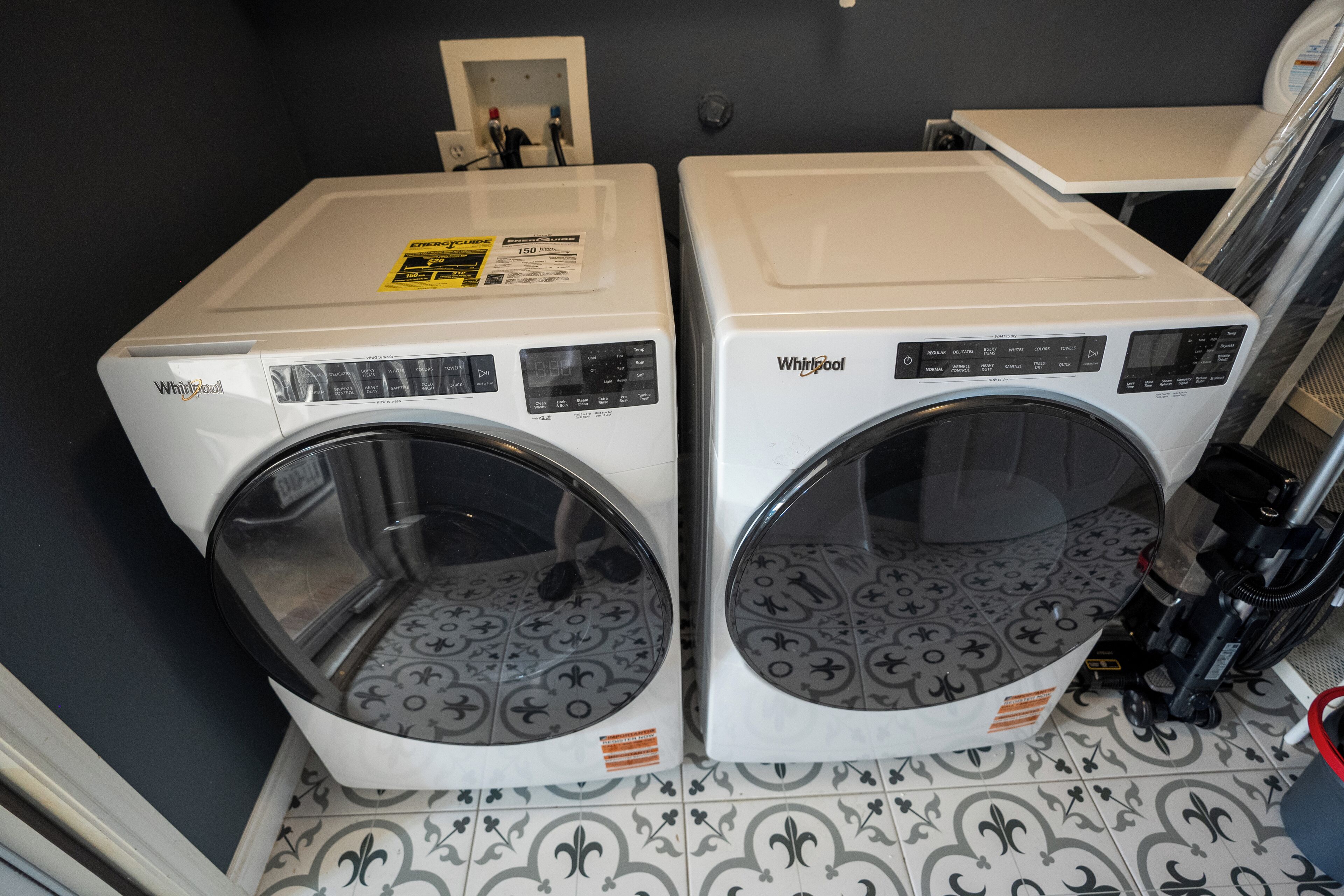 Deux lave-linge Whirlpool à chargement frontal se trouvent dans une buanderie dont le sol est recouvert de carreaux décoratifs.