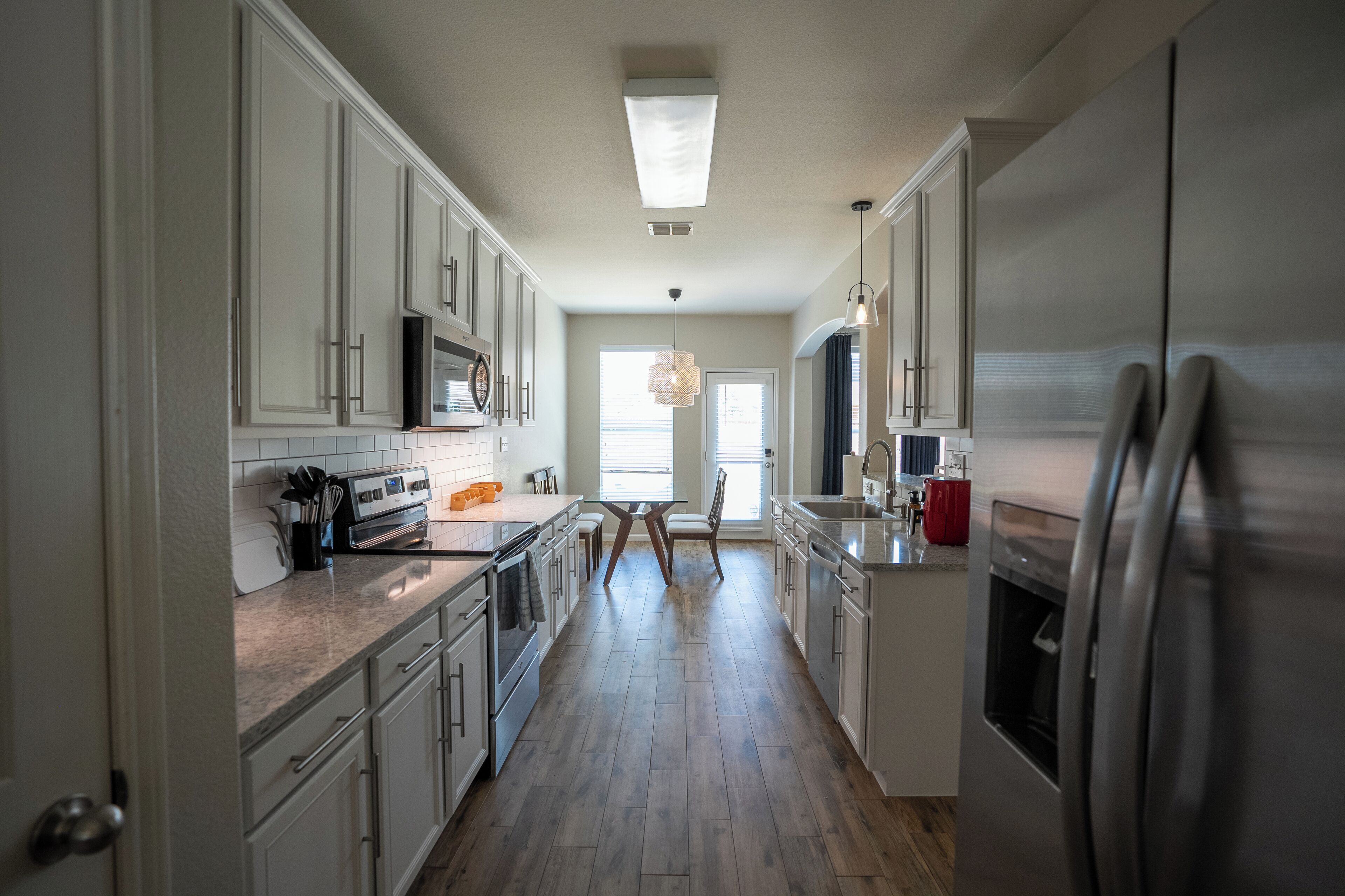Una cocina con armarios blancos, un refrigerador de acero inoxidable y piso de madera.