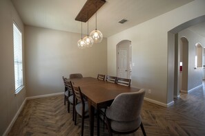 A dining area with a wooden table, six chairs, and three pendant lights.