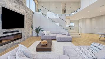 A spacious living area with a large flat-screen TV, a fireplace, and a modern staircase.