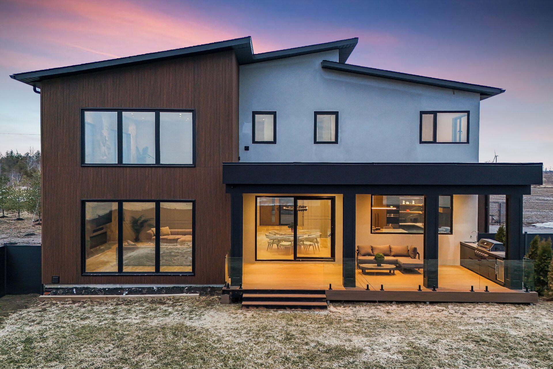 A modern two-story house with large windows and a dining area visible through the glass doors.