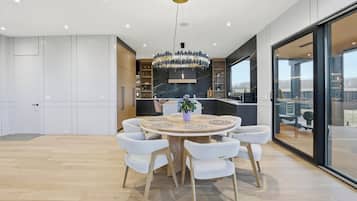A modern kitchen with a central island, a dining area with a round table and chairs, and a large window offering a view.