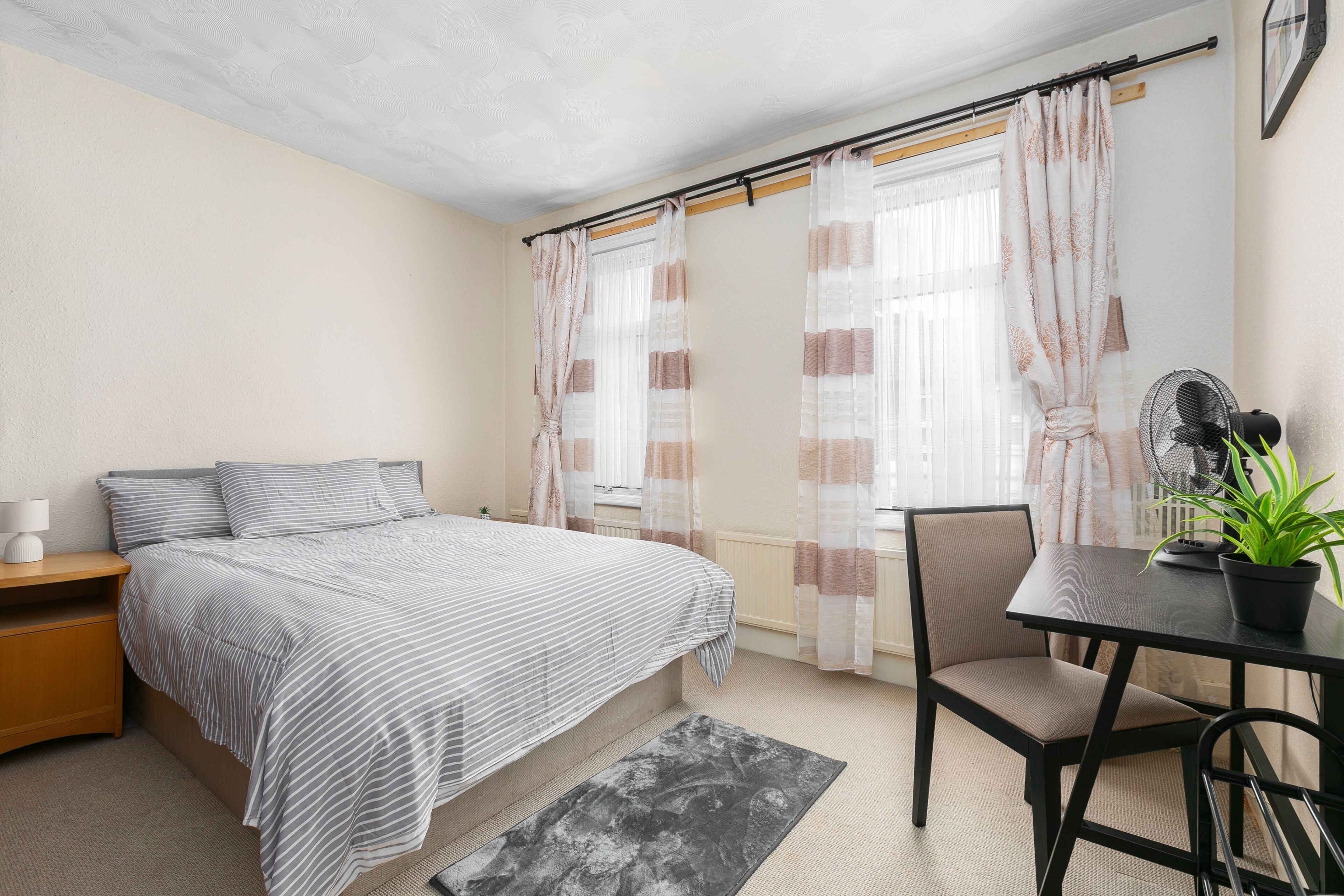 A bedroom with a bed, bedside table, chair, and a small table with a plant.